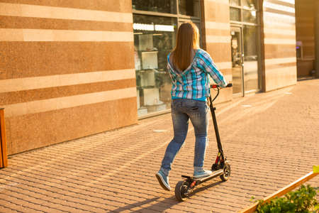 Smiling woman is standing on a scooter in the city