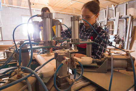 Experienced craftsman teaching female apprentice to work with woodworking machinery