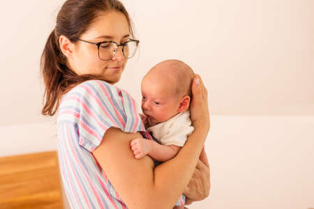 Young tired mother holding her newborn baby on her shoulderの写真素材