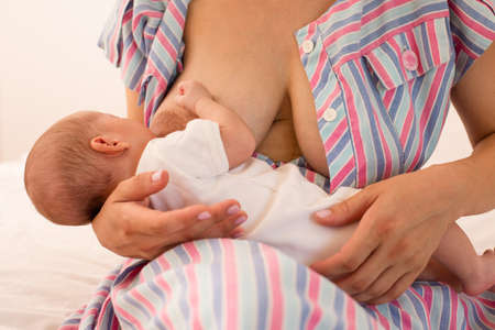 The mom is breastfeeding her newborn baby on the bedの写真素材