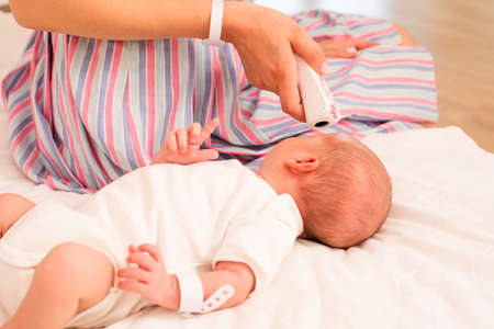 Mother measures newborn baby temperature on the bedの写真素材