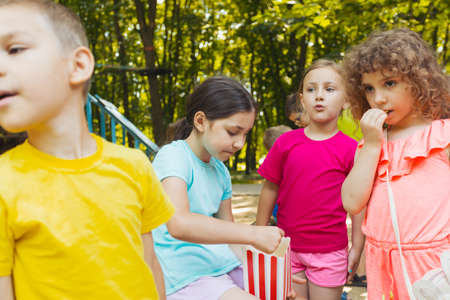 The kids are eating popcorn together in the park