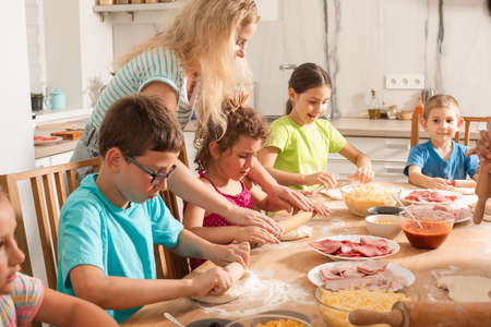 the teacher is learning children to cook pizzaの写真素材