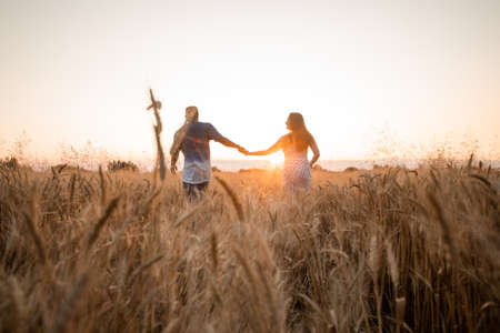 Mixed race young adult couple holding hands while walking in fieldの写真素材