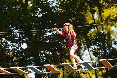 The concentrated girl carefully overcomes obstacles in the rope park