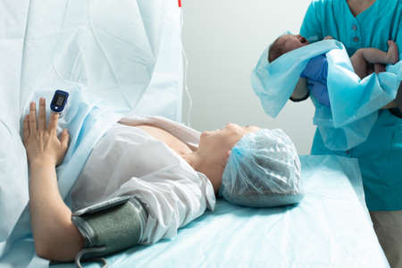 Nurse holds newborn baby close to mother in hospital