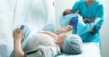 Nurse holds newborn baby close to mother in hospitalの写真素材