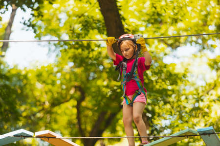 The concentrated girl carefully overcomes obstacles in the rope parkの写真素材