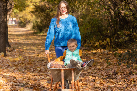 Mother have fun time with kid, use garden wheelbarrow with pumpkinsの写真素材