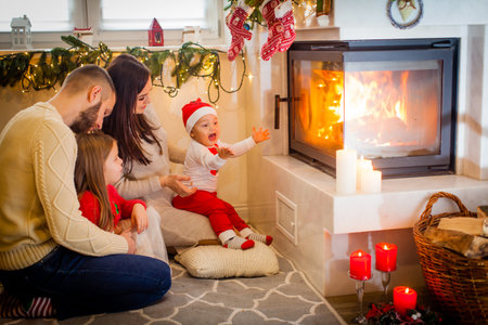 happy family father mother and children sitting by fireplace on Christmas Eveの写真素材