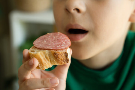 Boy eats sandwich. Focus on the food and face on backgroundの写真素材