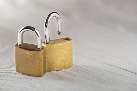 Two padlock, lock and unlock, with silvered keys on white wooden background. Estate and security concept with symbol of protection.の写真素材