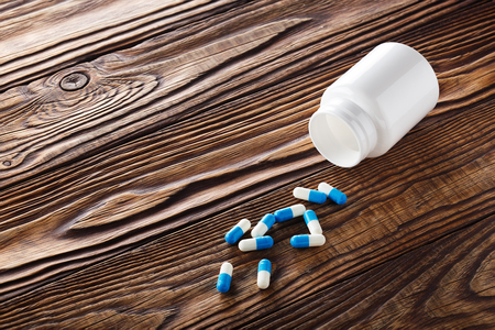 Medical blue pills and white bottle on wooden background.の写真素材