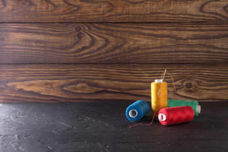 Sewing thread on coils, fabric, needles for sewing on wooden background. Set for tailoring products,...