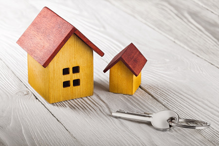 Real estate concept with wooden house and key on white wooden background. Idea for real estate concept, personal property and family house.の写真素材