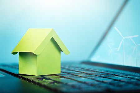 Green house on keyboard and wind power plants on computer screen. Smart house, ecology power, real estate, renewable energy concept.の写真素材