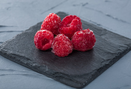 three big red raspberries on black stoneの写真素材
