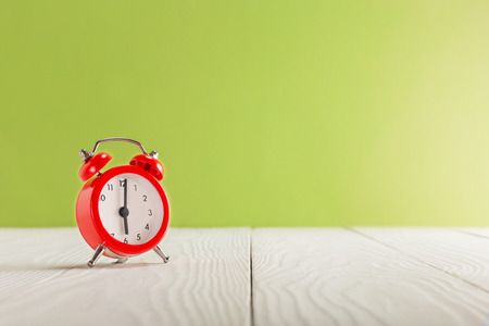 Clock on light wooden table with colorful background. Time for wake up.