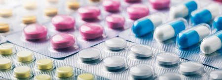 Heap of medical pills in white, blue and other colors. Pills in plastic package. Panoramic banner...