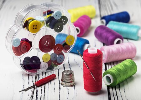 Hobby . Sewing threads and buttons with a needle and a thimble on a wooden table.