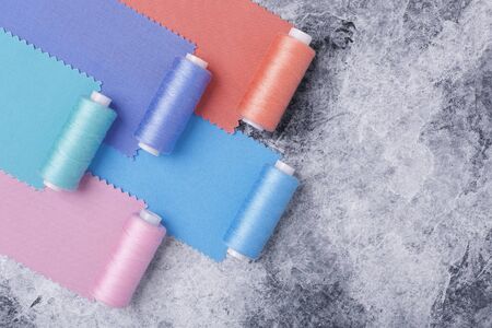 Colorful threads on bobbins and samples of colored fabrics, sewing kit. On a gray concrete background. Place for texの写真素材