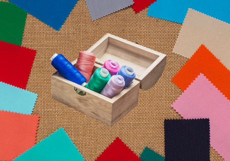 A small wooden box with threads on spools against a background of colored scraps of fabricの写真素材