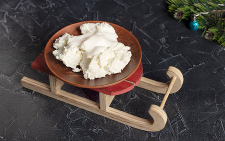 A large bowl with homemade cottage cheese and sour cream on a small wooden New Year's sleigh...