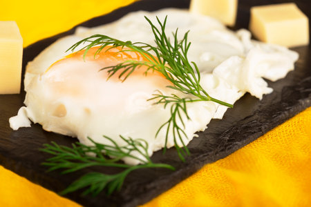 fried egg with herbs and cheese on a black stoneの写真素材