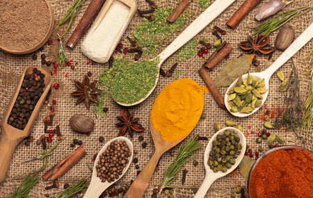 Background of multi-colored spices in spoons: turmeric, paprika, black and white pepper on rough burlap.の写真素材
