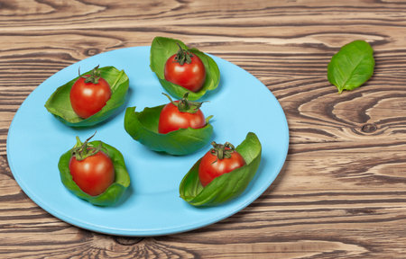 on a wooden background a blue plate with green basil and cherry tomatoesの写真素材
