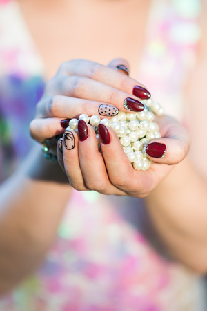 beautiful hand of a young woman with brown manicure holding white pearl necklaceの写真素材