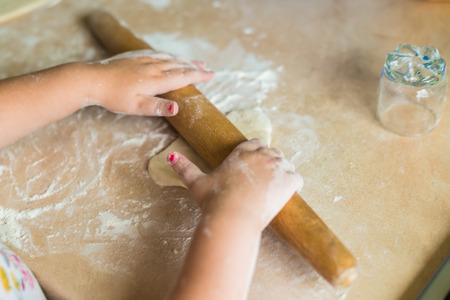 Children's hands holding a rolling pin and roll the dough on the table
