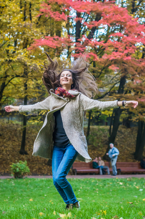 smiling, happy girl jumping on green grass in autumn parkの写真素材