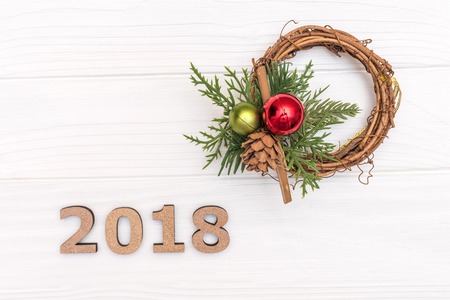 The numbers 2018 and wreath of pine branch and cone on white wooden background