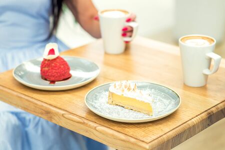 Two cups of coffee and two different pieces of cake on the background of a girl with a cup of coffee.の写真素材