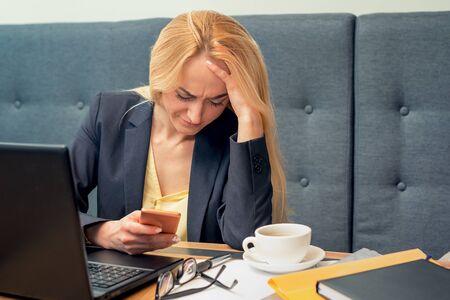 A beautiful business woman is looking at smart phone with feeling sad at modern cafe. Business...