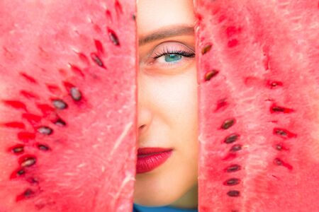 Close-up portrait of part of the girl's face between two pieces of watermelon. Girl is looking out between two pieces of watermelon.の写真素材