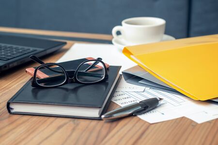 Side view glasses , smartphone, laptop, note book and pen on the wooden table. Selective focus office table. Business conceptの写真素材