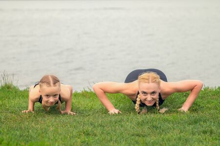 woman and child are training near the lake on the green grass, sporty mother and daughter, fitness, yogaの写真素材