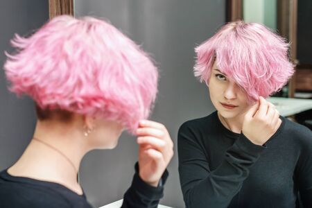 Pink hair woman with a short hair is looking at the mirror. Beauty concept.の写真素材