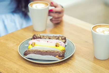 Different sweet pieces of cakes on plates. Breakfast in cafe. On background hand of woman are holding cup of coffee.の写真素材