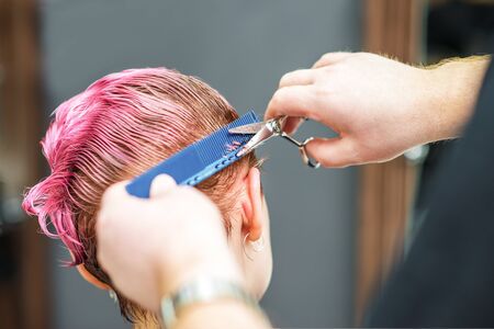 Closeup of hands are cutting client's wet pink hair at hair salon. Hairdresser cuts woman's hair. Barber hands cuts pink hair.の写真素材