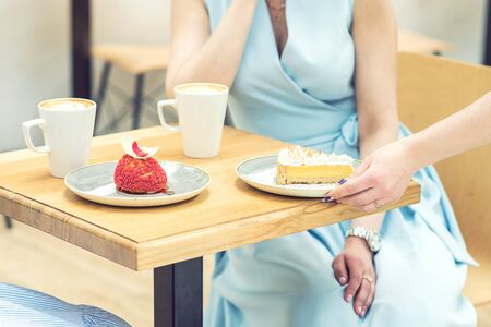 The female hand puts the piece of cake on the table at cafe. Woman hand is putting slice of cake on the table on background of female in blue dress.の写真素材