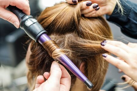 Professional hairdresser is twisting the hair with a curling iron in beauty salon close up. Concept...
