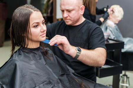 Hair stylist is making new hairstyle for beautiful young woman in hair salon.