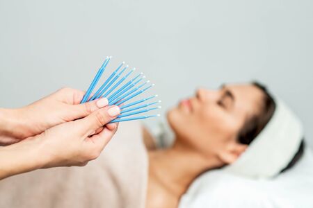 Eyelash extension disposable microbrushes, eyelash cotton swabs in hands on backgrond of patient, close up.の写真素材