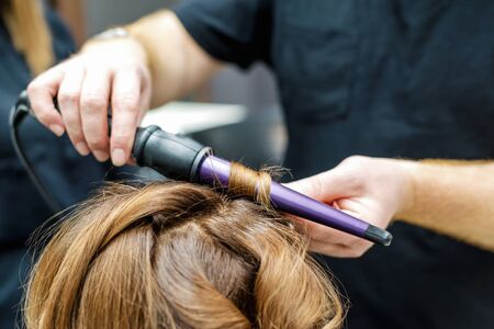 Professional hairdresser twisting the hair with a curling iron in beauty salon, close up.