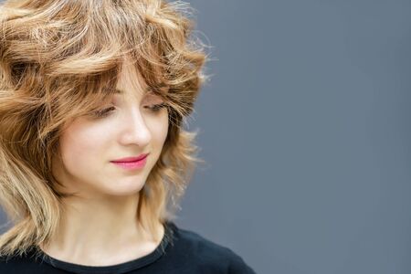 Young woman with brown curly hairstyle on gray background, copy space.