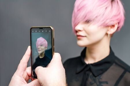 Male hands photographing pink short hairstyle of young woman on a gray background.の写真素材