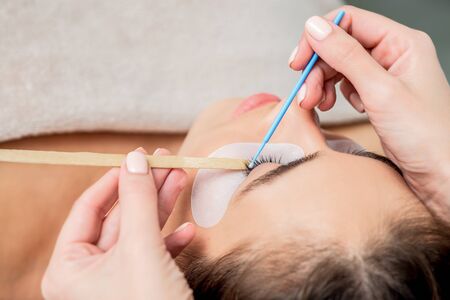 Beautiful woman receiving eyelash extension procedure, close up.